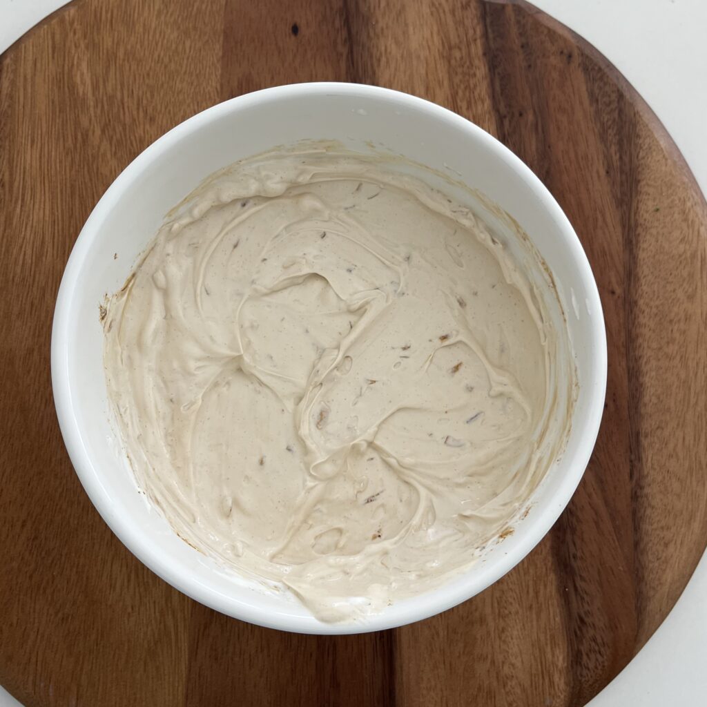 Mixed onion dip in a white bowl on a brown cutting board on the counter.