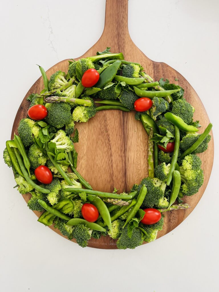 Green vegetables in a wreath shape on a brown board on the counter.