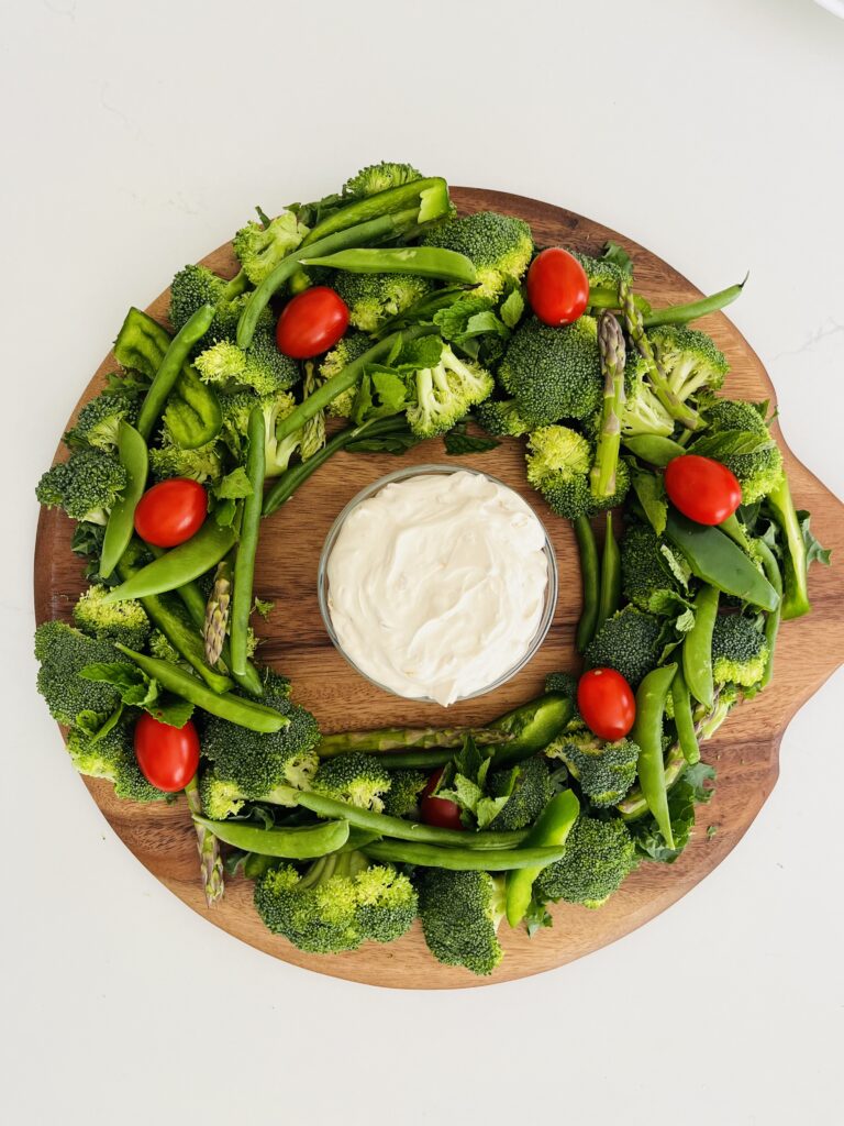 Holiday Vegetable Wreath on a brown board with onion dip in the center of it. On the counter.