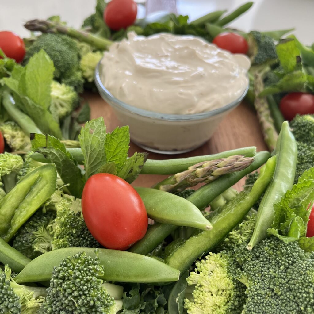 Effortless Onion Dip on a brown board surrounded by assorted vegetables on the counter.