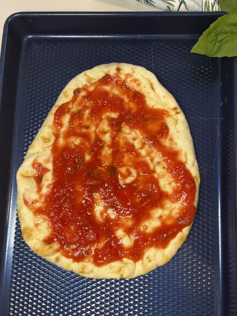 naan bread with tomato sauce on a blue baking sheet on the counter.