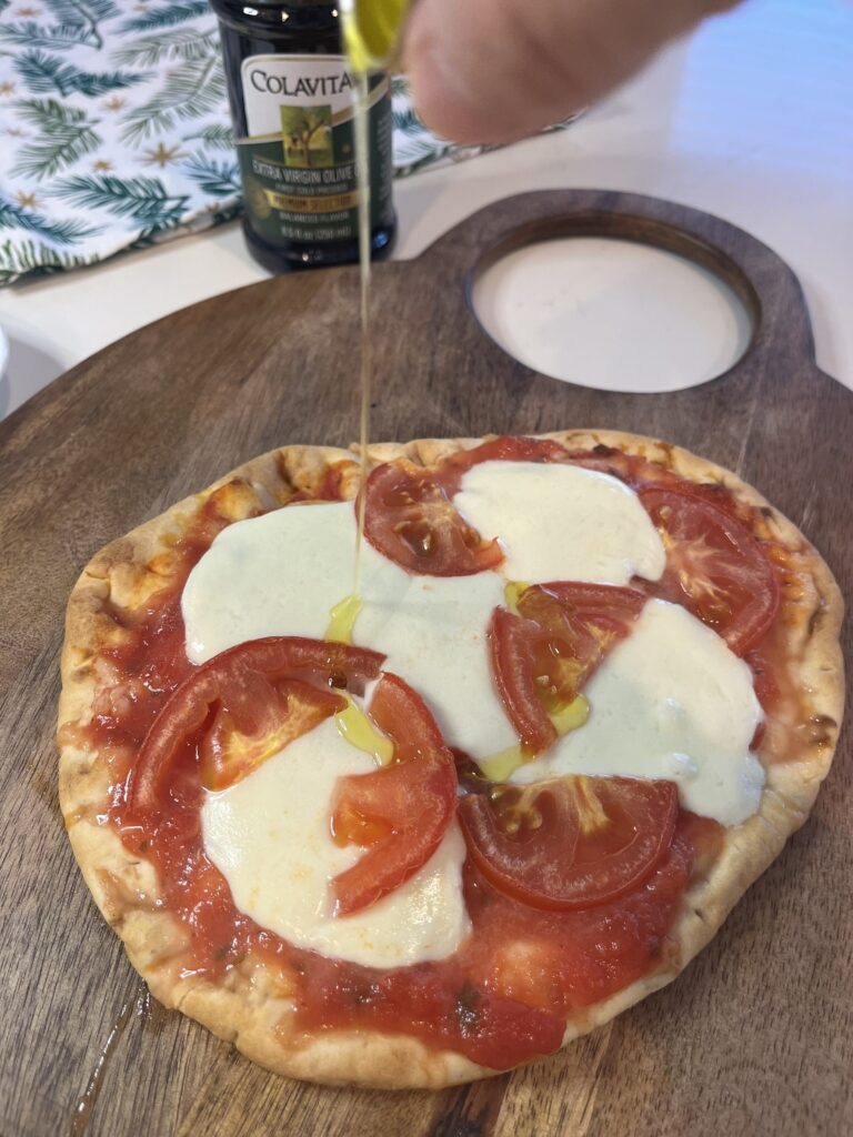 Drizzling olive oil onto the pizza on a brown cutting board on the counter.