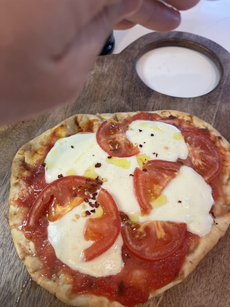 sprinkling red pepper flakes on the pizza on a brown cutting board on the counter.