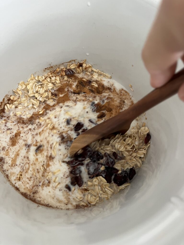 Stirring with a wooden spoon all of the ingredients in a slow cooker on the counter.