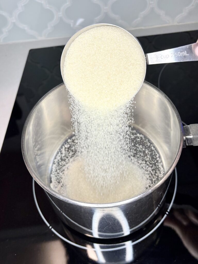 sugar being added to an empty saucepan on a stove