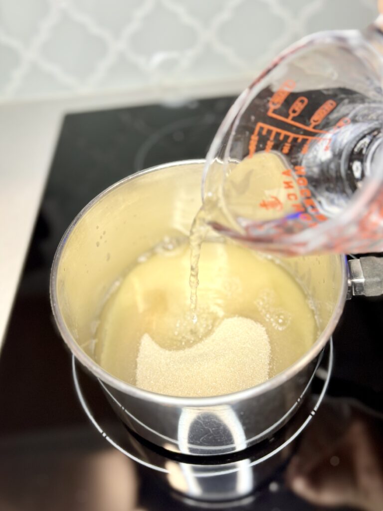 water being added to sugar in a saucepan on a stove