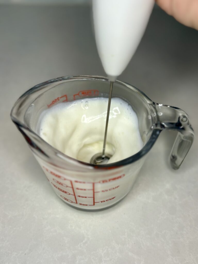 milk being frothed in a measuring cup