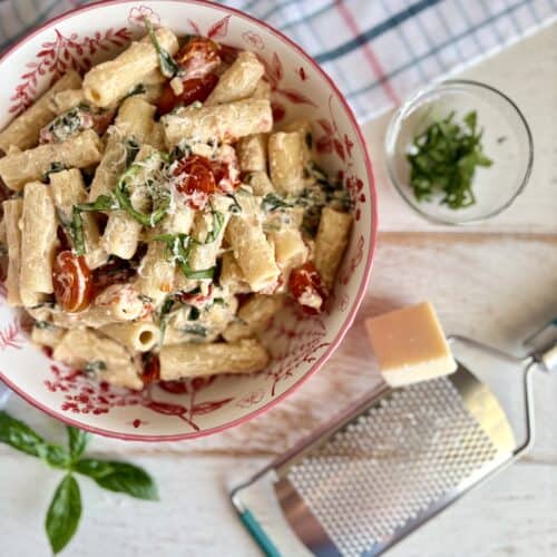 Baked Boursin pasta in a dish next to a cheese grater with parmesan and fresh basil