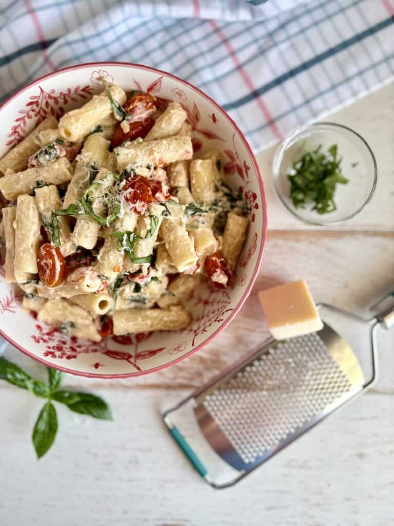 Baked Boursin pasta in a dish next to a cheese grater with parmesan and fresh basil