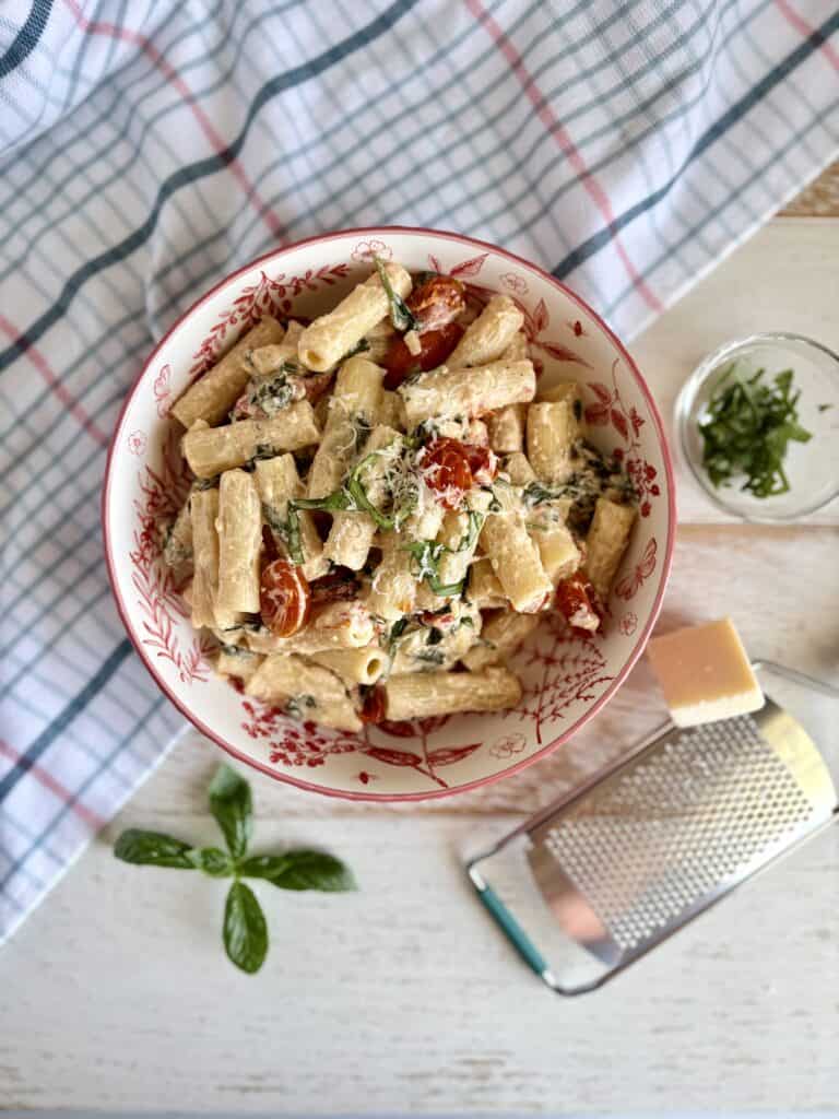 Baked Boursin pasta in a dish next to a cheese grater with parmesan and fresh basil