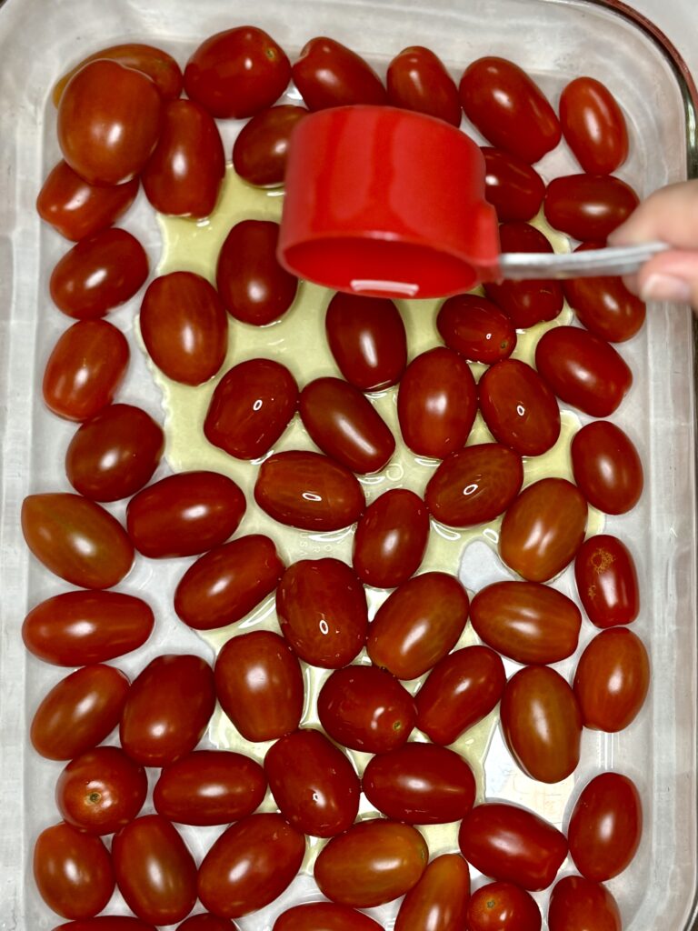 olive oil being poured over grape tomatoes in a baking dish