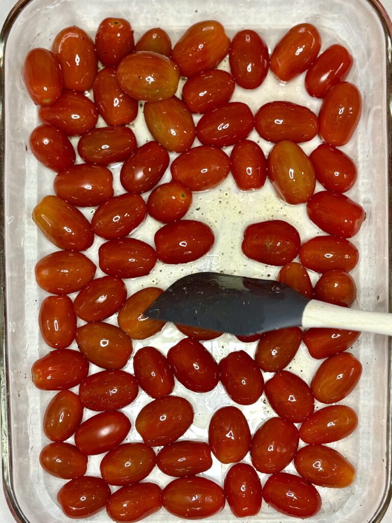 tomatoes, oil, salt and pepper being stirred in a baking dish