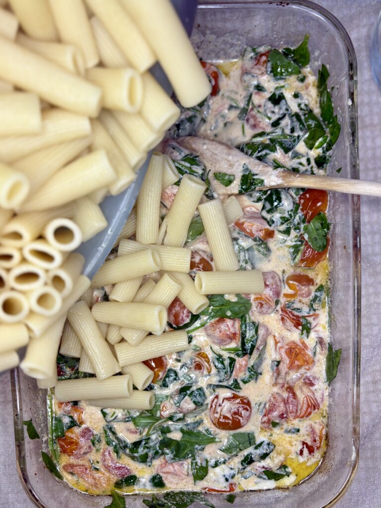 pasta being added to tomato, cheese, spinach mixture 