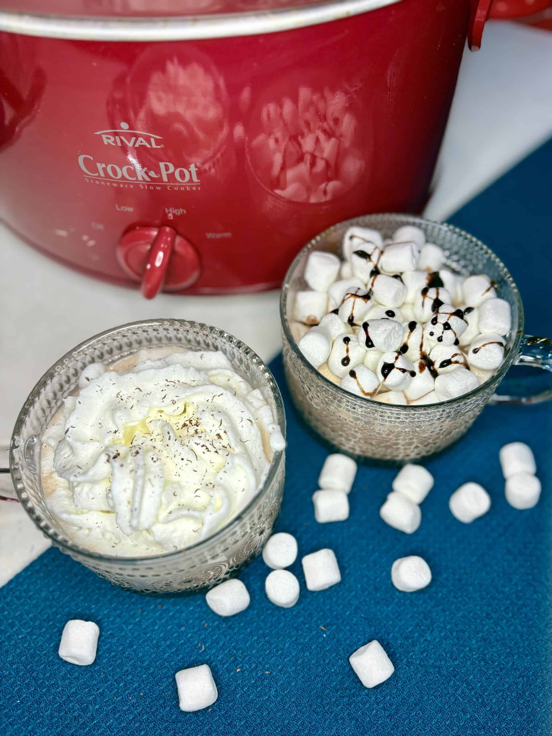 2 mugs of hot cocoa on a counter with a slow cooker