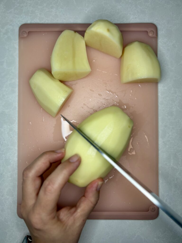 potatoes being cut into quarters on a cutting board