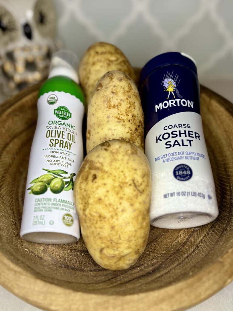 raw potatoes, salt, and olive oil spray in a bowl on a counter