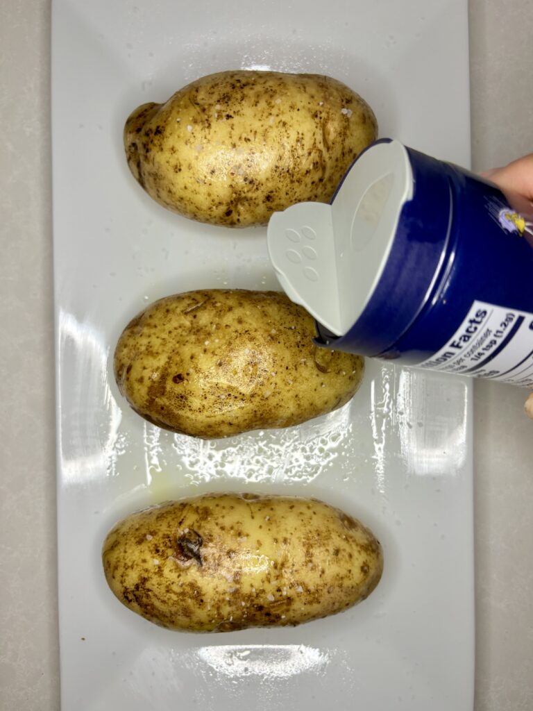 salt being sprinkled onto potatoes on a plate