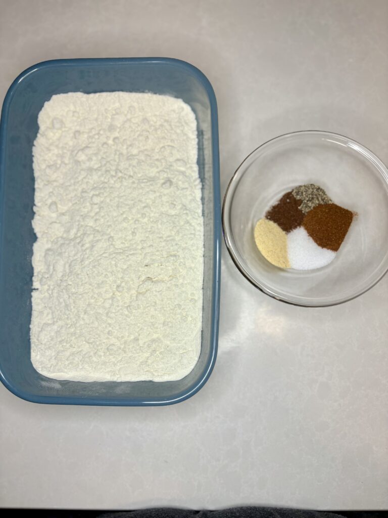 flour in a pan next to a bowl with the seasoning on a counter