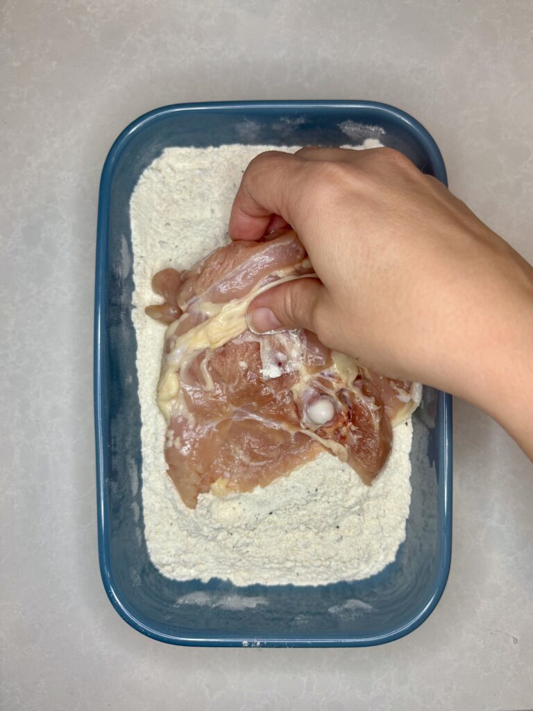 chicken thigh being dredged in flour