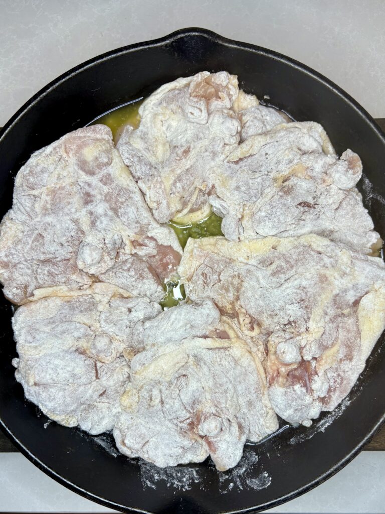 floured chicken thighs in a skillet with melted butter