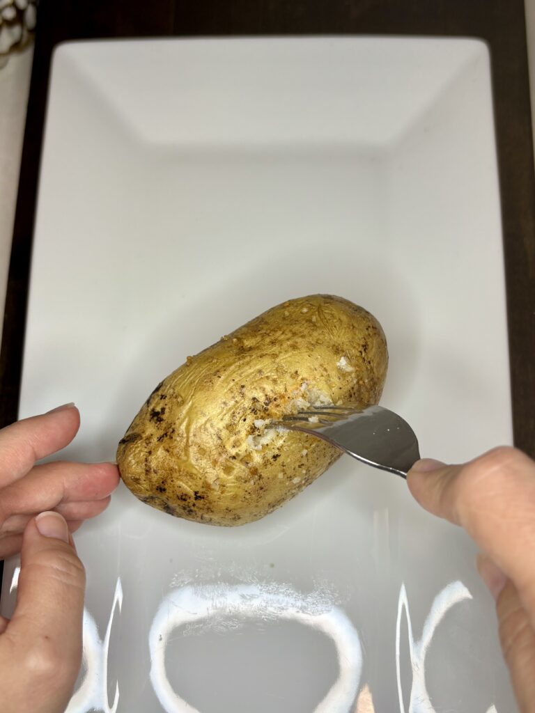 a fork making a slit down the middle of a potato on a plate 