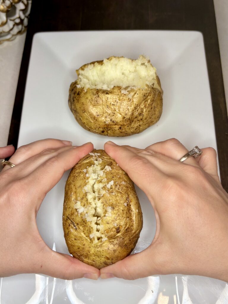 2 hands squeezing a potato to pop open seam