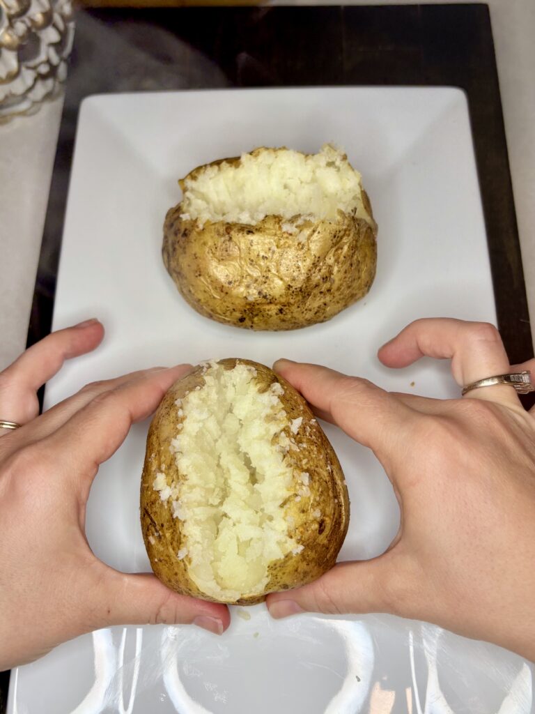 a popped open potato with 2 hands on a plate