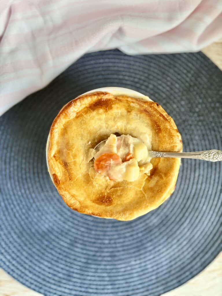 Homemade baked chicken pot pie with a spoon on a blue placemat next to a pink kitchen towel