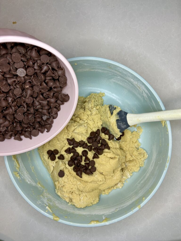 chocolate chips being stirred in to dough in bowl