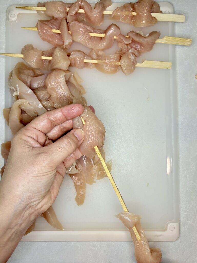 raw chicken breast strips being threaded onto skewers