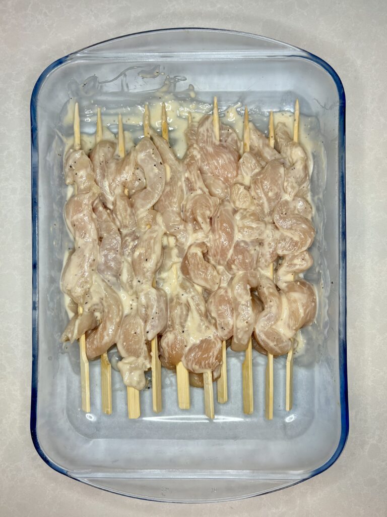 raw chicken breast skewers marinating in a dish with caesar dressing