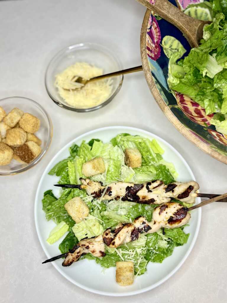 chicken skewers on top of lettuce in a meal bowl with cheese and croutons