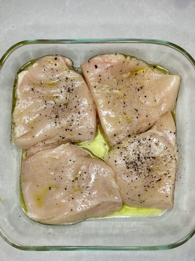 chicken pieces in a glass dish topped with oil, vinegar, salt, and pepper