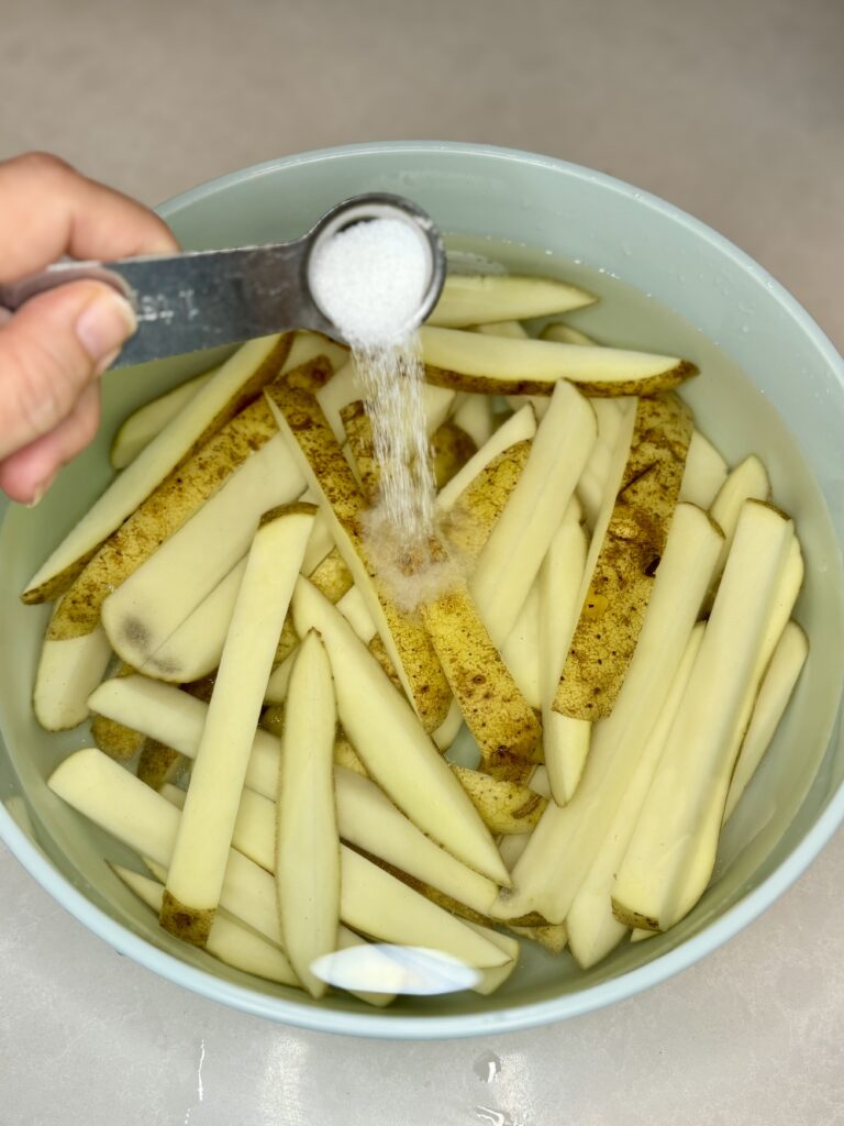 salt being poured into a bowl with potatoes and water