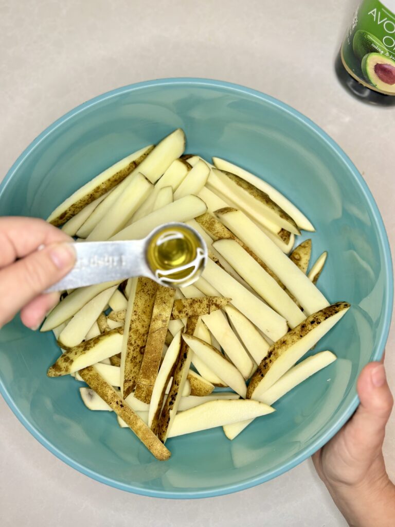 oil  being poured onto uncooked fries in a bowl