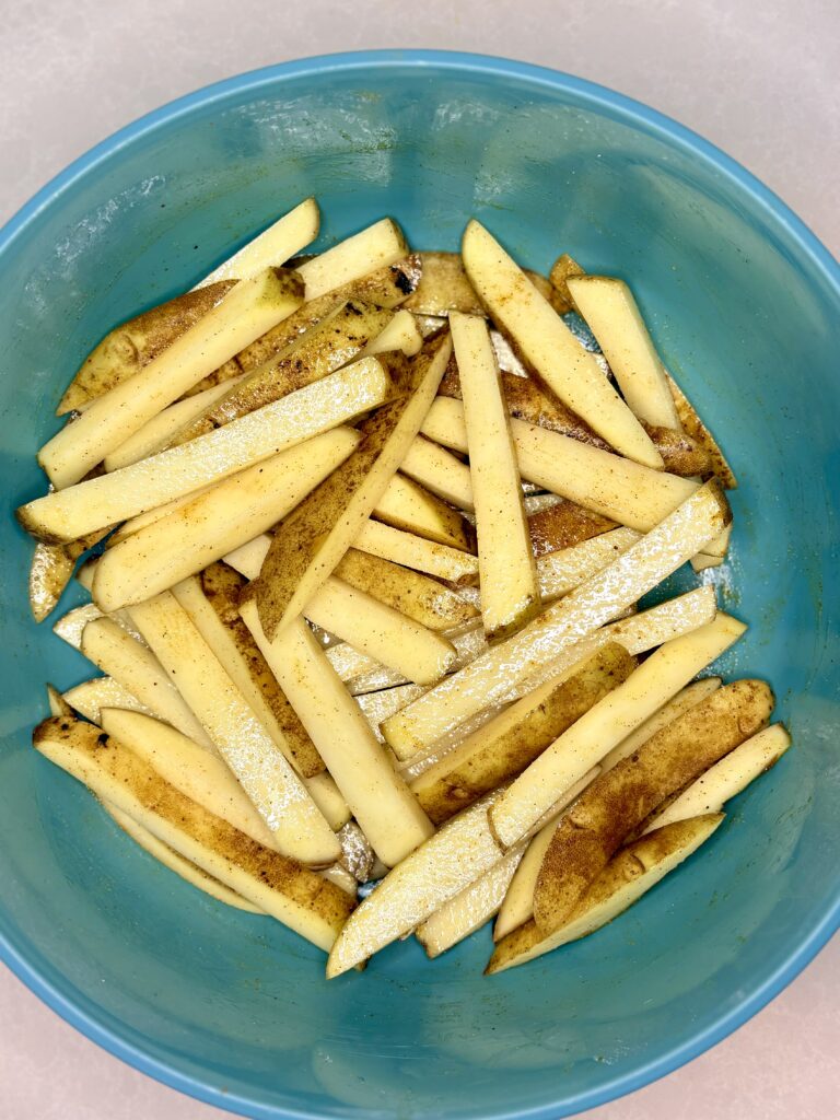 uncooked fries in a bowl with oil and seasoning 