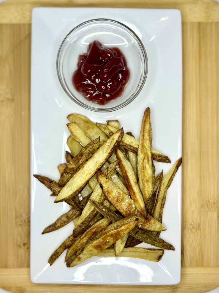 cooked fries on a plate next to a bowl of ketchup 