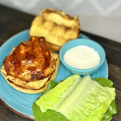 bufalo chicken on a grilled bun on a plate next to lettuce and a bowl of dressing