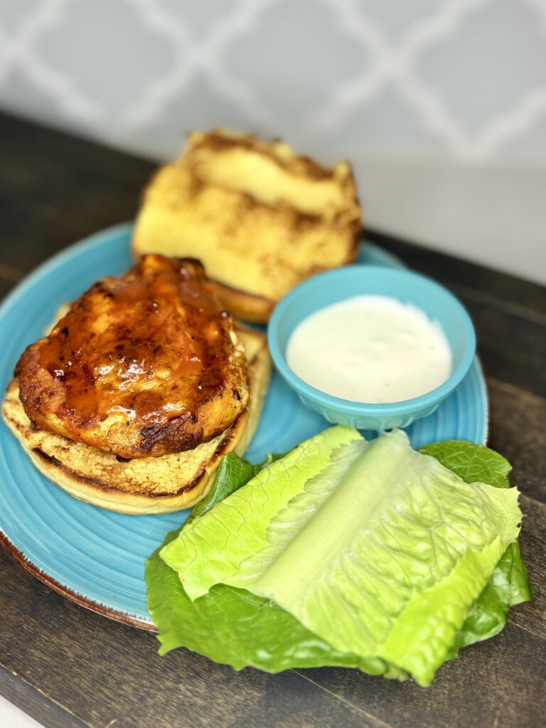 bufalo chicken on a grilled bun on a plate next to lettuce and a bowl of dressing