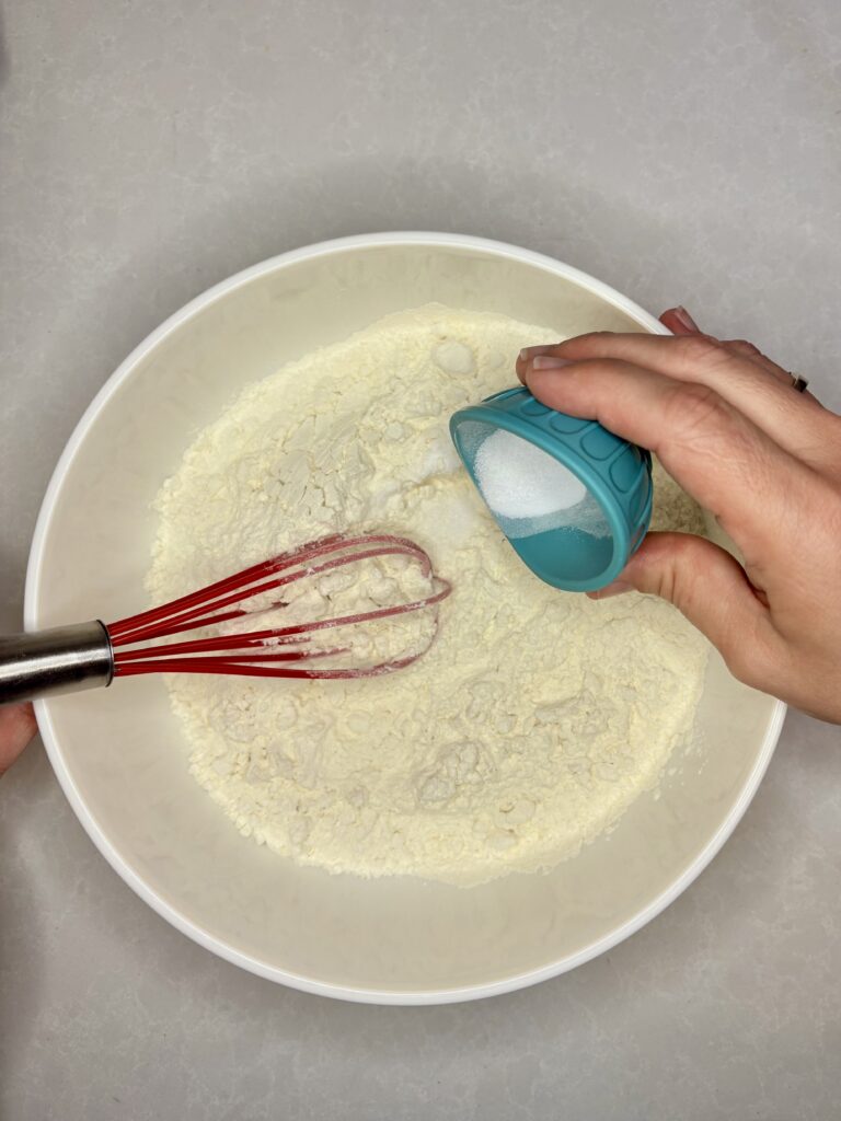 salt and baking soda being whisked into flour in a bowl