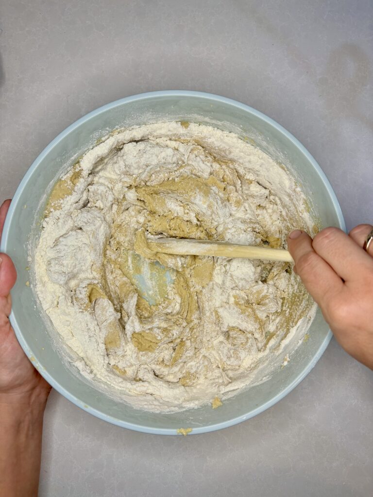 flour being stirred into dough with a wooden spoon