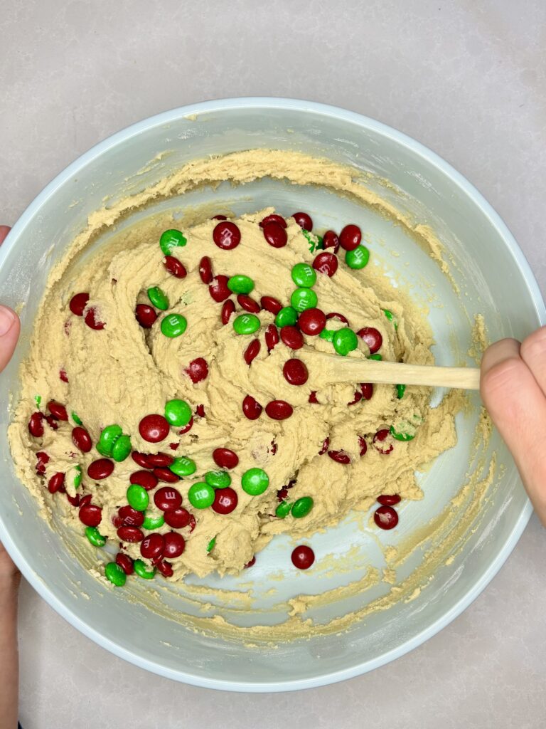 m and m's being stirred into dough with wooden spoon