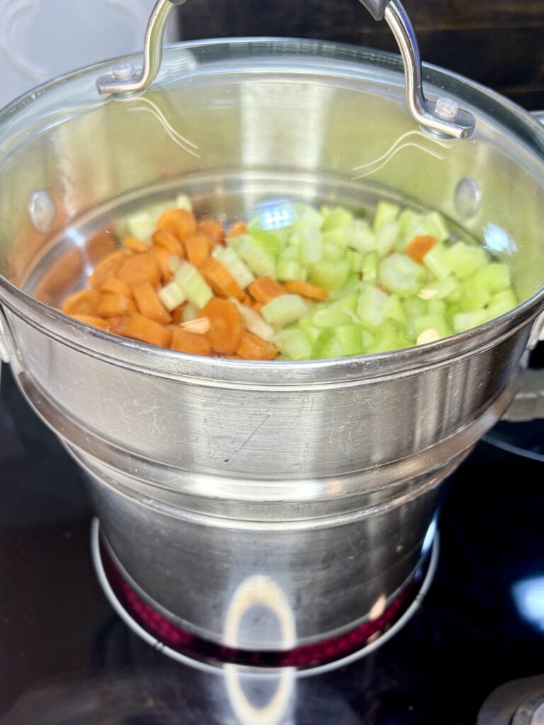 carrots and celery in a steamer basket over a pot of water on a stove