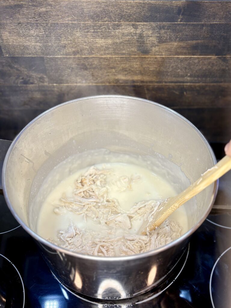 cooked shredded chicken being stirred into pot