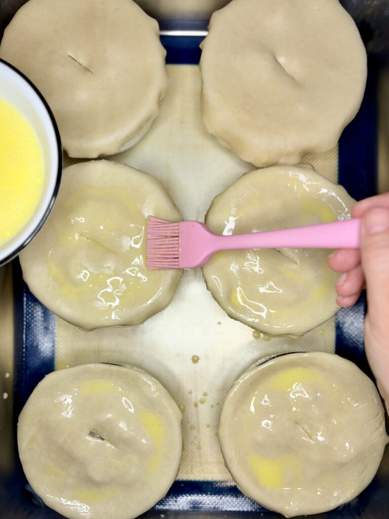 egg wash being brushed onto pie curst over small dishes