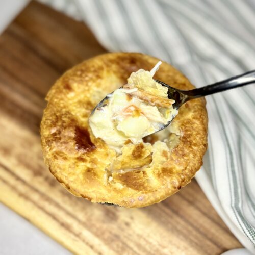 chicken pot pie in an individual baking dish on a board on a counter next to a towel