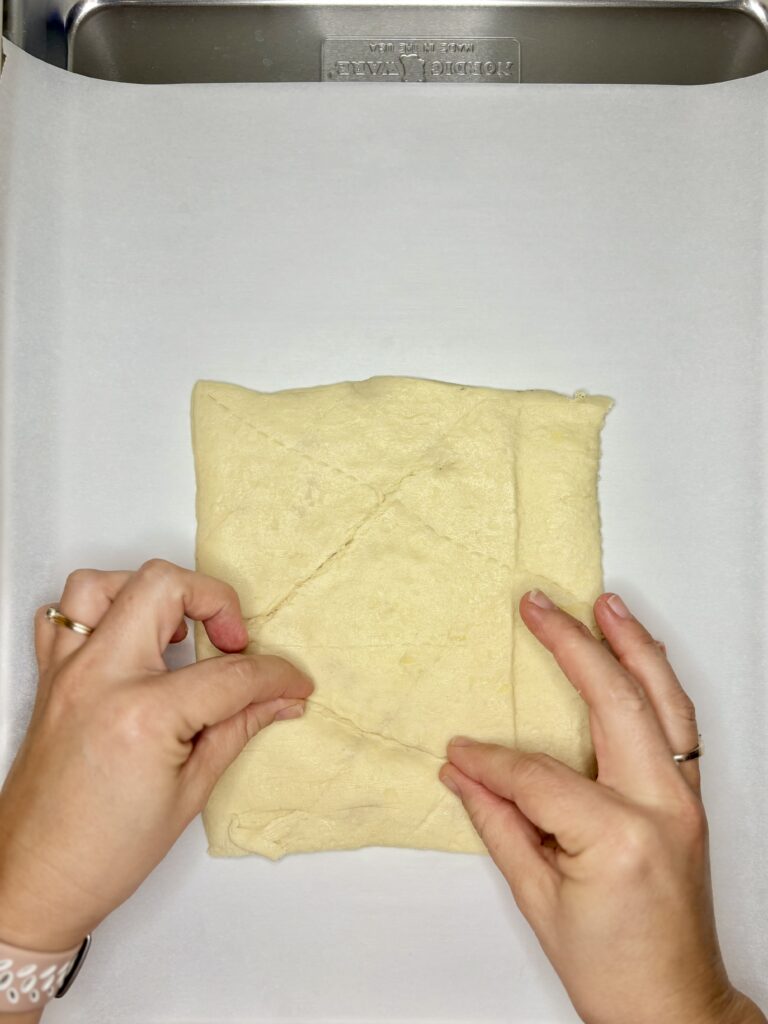 four crescent roll triangles being pinched together on a baking sheet lined with parchment paper