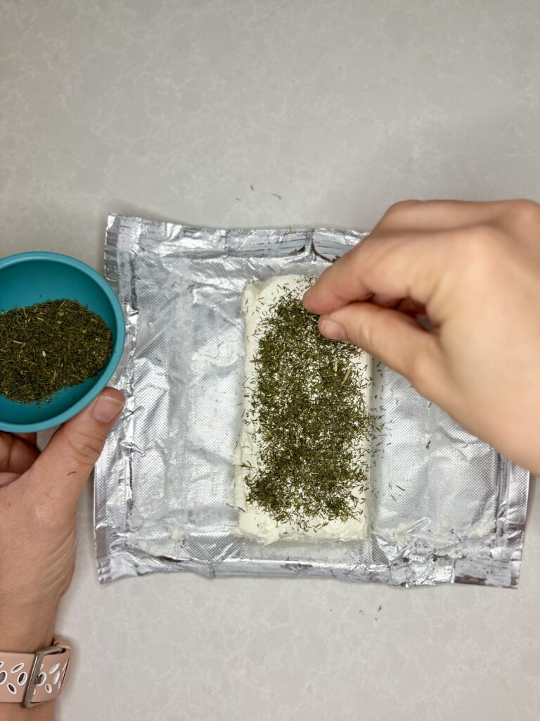 dried dill being sprinkled on to a block of cream cheese