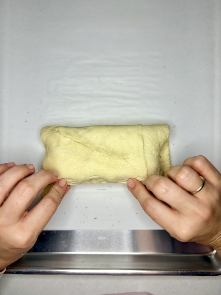 crescent roll dough folded over cream cheese and being pinched together 