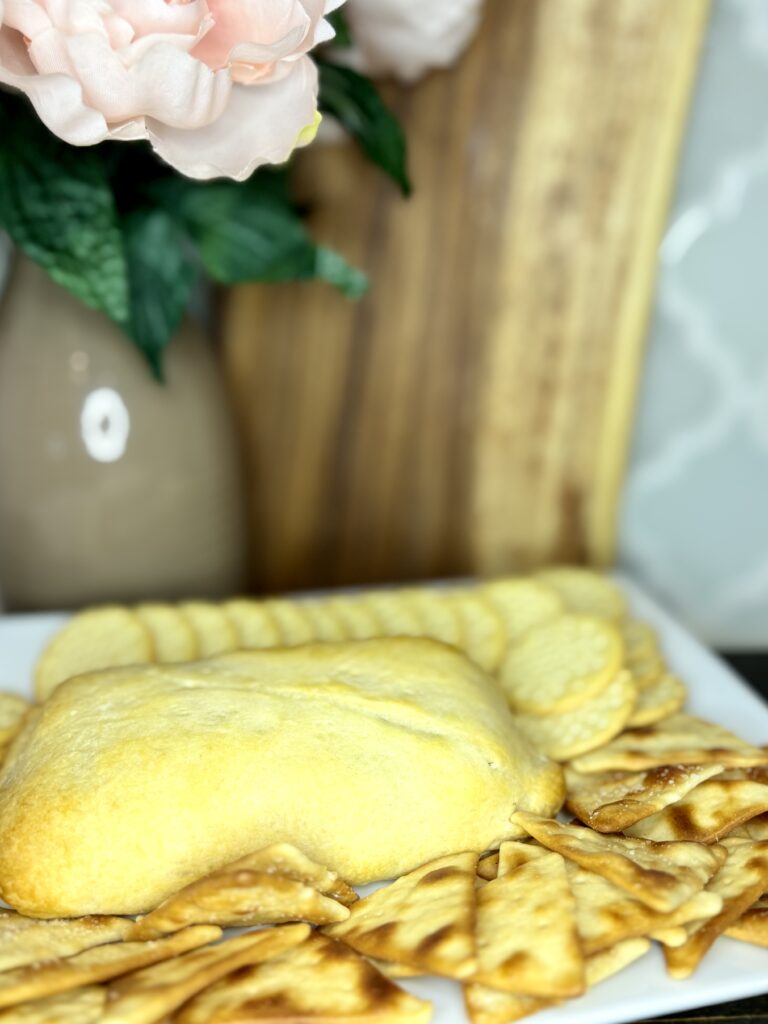 baked creamy dill dip on a plate with crackers and pita chips on a counter